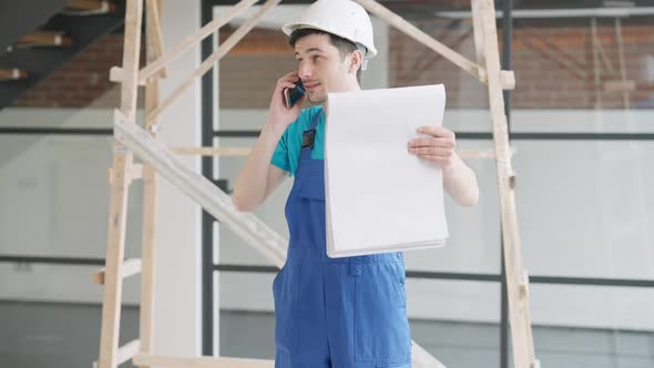 Confident Young Man in Hard Hat Talking on the Phone Holding Drawings