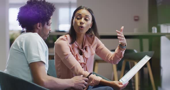 Video of focused diverse businesswoman and businessman with papers talking