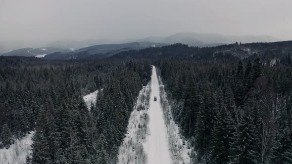 Aerial View From Drone on Car Driving Through Winter Snow Covered Forest