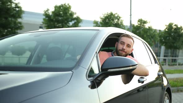 A Young Man with Beard Looks Out of the Car Window Smiles and Gives Thumbs Up