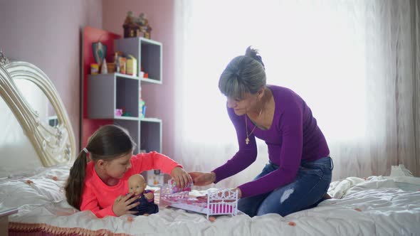 Mom and daughter play dolls on the bed. Mother's Day