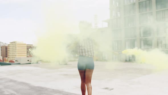 Fashionable young woman on urban rooftop using smoke grenades