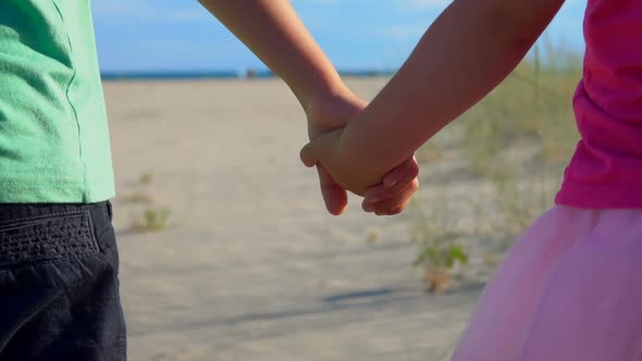 Closeup of Little Boy and Girl in Pink Skirt Holding Hands on the Beach