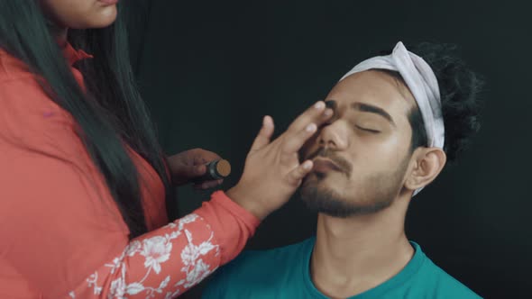 Close up of make up artist putting a make up products on man's face in cosmetics studio