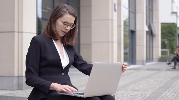 Woman in Formal Attire Using Laptop Outside Office Building