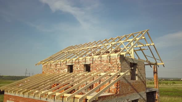 Aerial view of unfinished brick house with wooden roof frame structure under construction.