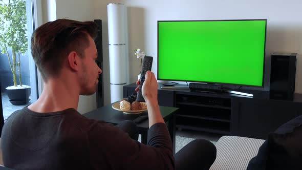 A Man Clicks with a Controller at a TV with a Green Screen and Shakes His Head Unhappily