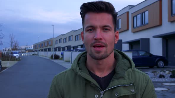 A Young, Handsome Man Talks To the Camera About a Street and Buildings Behind Him