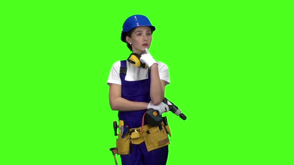 Builder Girl in a Helmet and Overalls Holds a Drill in Her Hands . Green Screen. Slow Motion