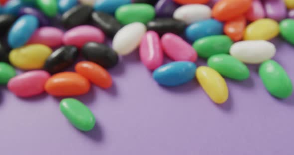 Video of close up of multi coloured sweets with copy space over purple background