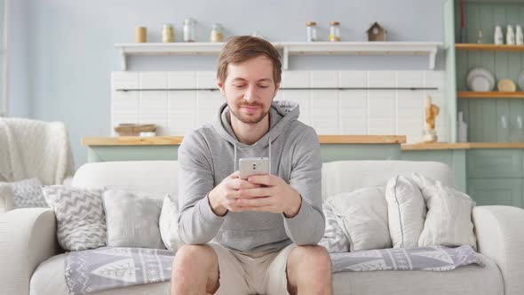 Hipster young man using his smart phone while sitting on the couch at home