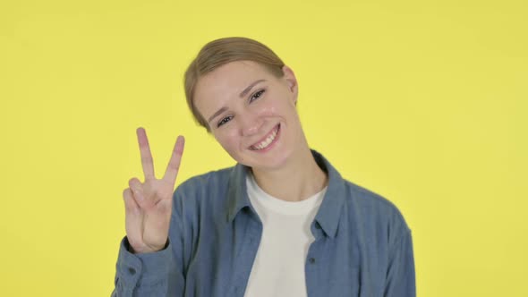 Young Woman Showing Victory Sign on Yellow Background