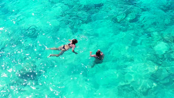 Two beautiful young females swimming in the crystal clear waters of a paradise beach island