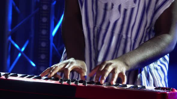 African American Man Plays Piano Synthesizer and Sings in Dark Studio with Blue Lights