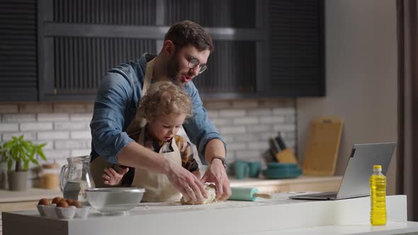 Young Man and His Little Son are Cooking on Kitchen and Talking By Video Chat in Laptop with Someone