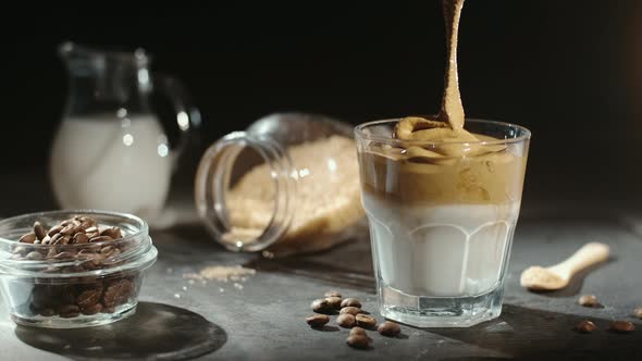 Making dalgona coffee with almond milk and brown sugar, coffee beans on black background