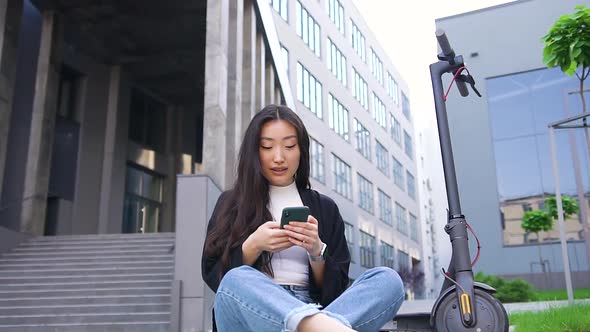 Young Asian Girl in Casual Clothes Sitting on the Asphalt  and Using Her Phone