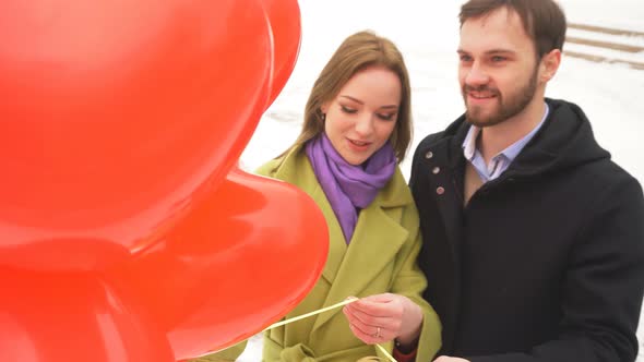 Man and a Woman in Love Walk Through a Winter Park During the Day Holding Orange Balloons in Their