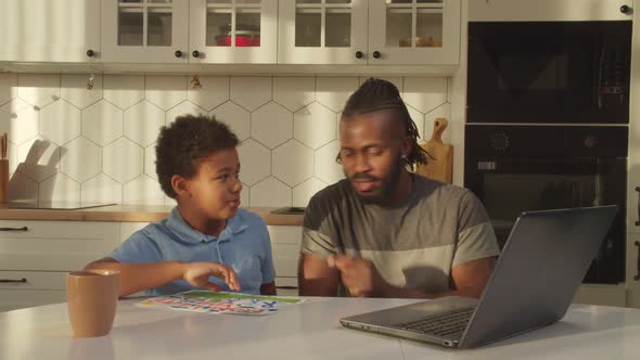 Joyful African Father and Cute Boy Making Video Call Online Using Laptop Indoors