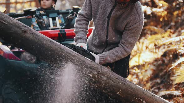 An Autumn Forest - Man Cutting Wood with a Chainsaw While His Kid Waits for Him in an ATV