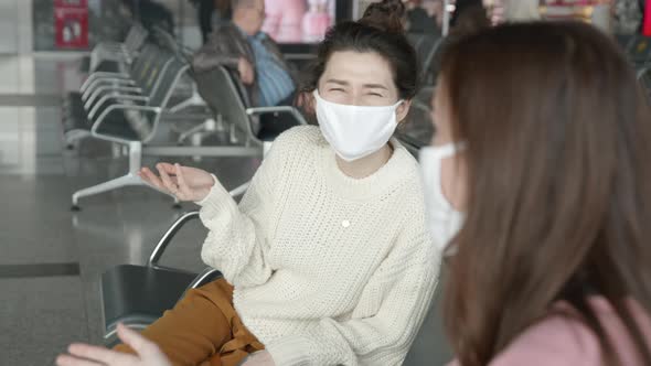 Two Women Tourists in Medical Mask Sitting in Airport Terminal at Safe Distance and Talking Before