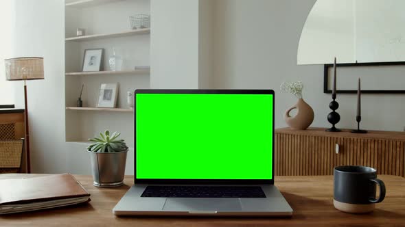 An Open Laptop with a Green Screen Standing on a Table in a Home Interior