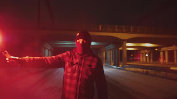 Man in Balaclava with Red Burning Signal Flare at Night