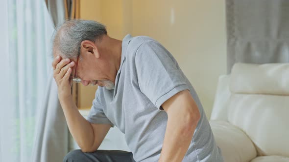 Asian Senior elderly mature man feel suffering from terrible headache while sit on sofa at home.