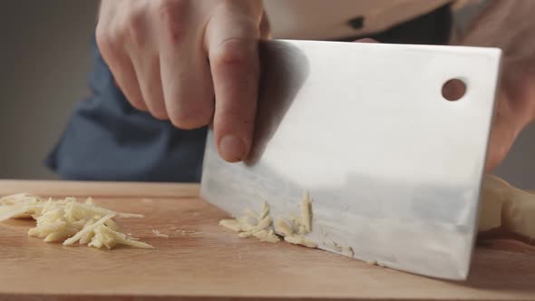 Front View of Young Man Chef Cut Thin Slices of a Piece of Ginger with Knife