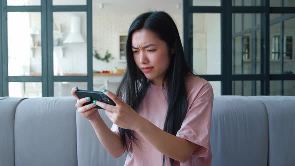 Excited Young Asian Woman Holding Mobile Phone and Playing Virtual Computer Games Enjoying Victory