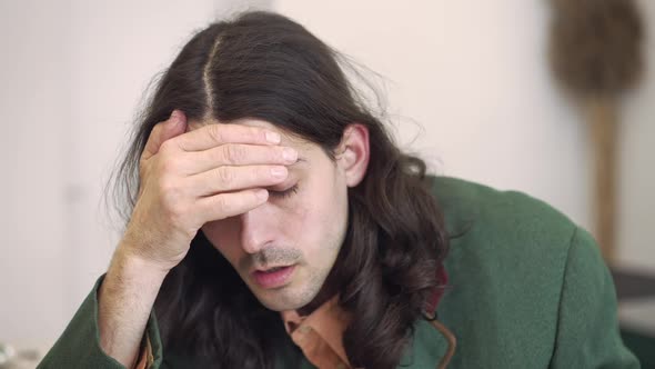 Headshot of Frustrated Young Handsome Brunette Man with Long Hair and Brown Eyes Drinking Coffee