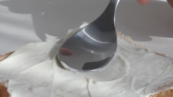 Spoon spreading cream cheese over the bread surface slow motion footage