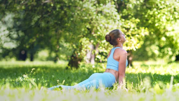 Lady athlete practices yoga pose Cobra and stretches back on green park