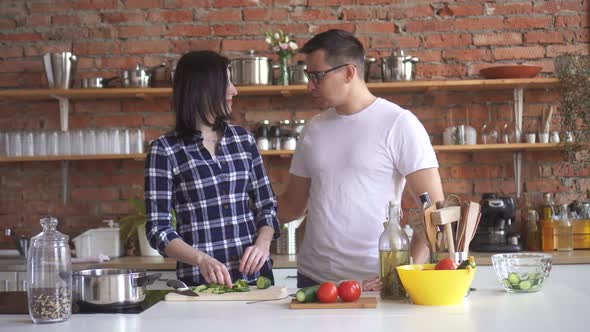 Portrait of a Young Couple in the Kitchengirl Cuts Vegetables and Gives a Man a Try