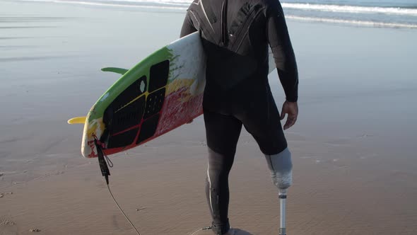 Back View of Male Surfer with Bionic Standing on Ocean Shore