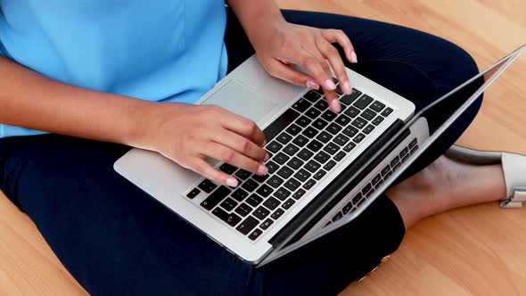 Female executive using laptop while sitting on wooden floor 4k