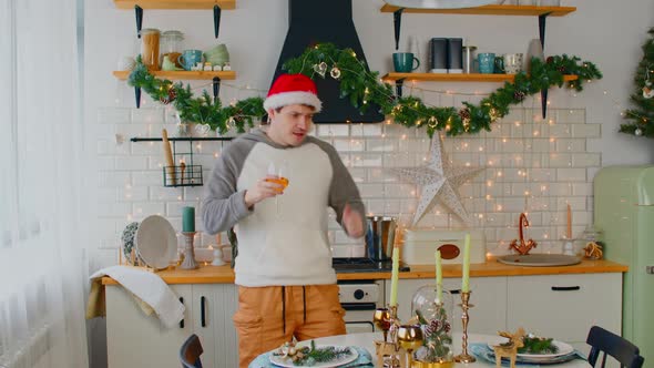 Young Man Wearing New Year Hat Drinking Wine and Dancing at Table