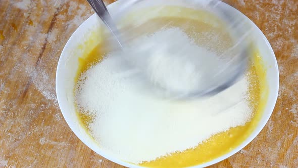 A Woman Sifts Flour Through a Small Metal Sieve Into a White Deep Bowl with Liquid Yellow Dough on a