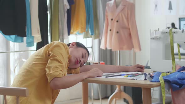 Back View Of Asian Female Designer With Sewing Machine Yawning And Sleeping While Designing Clothes