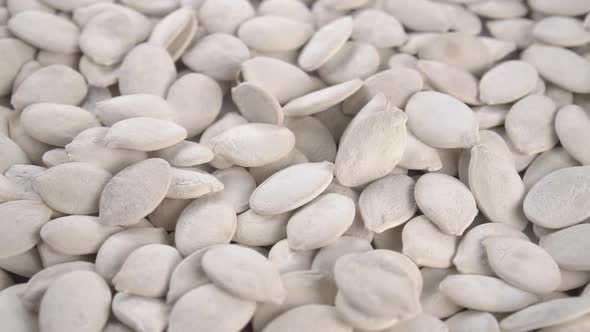 Dried salted unpeeled pumpkin seeds with shells fall into a heap in slow motion