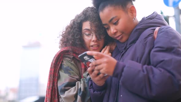 Two young women multiethic outdoor using smart phone