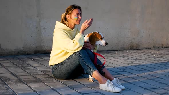 Ukrainian Refugee Woman with National Flag on Cheek Sitting Underground with Dog