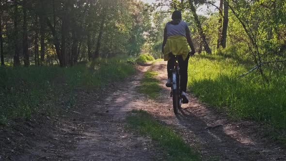 Young Woman on Bicycle Rides Along Green Forest Path in Summer Day Slow Motion