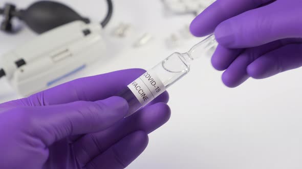 Transfer of coronavirus vaccine in a glass capsule. Hand in hand in medical protective gloves 