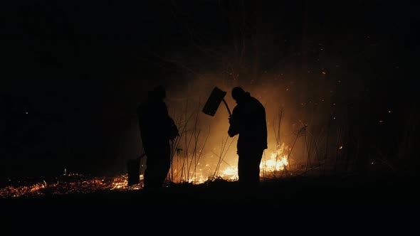 Two Firefighters with Fire Flappers Extinguish a Fire at Night