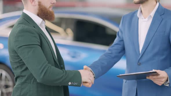 Unrecognizable Caucasian Dealer and Buyer Shaking Hands and Passing Car Keys in Dealership