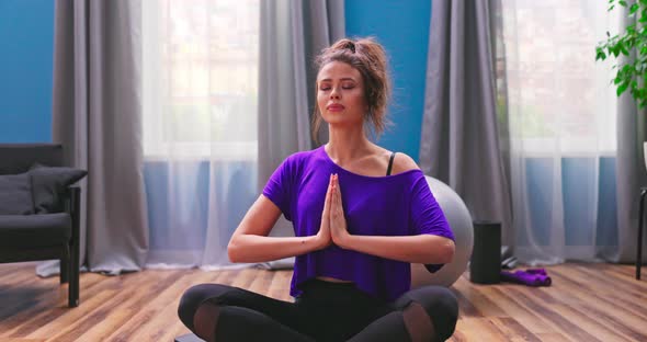 Portrait of Beautiful Young Woman Dressed in Fitness Clothes Meditates While Sitting in Lotus