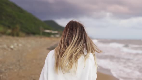 Backview Portrait of Blonde Woman Walking Along Ocean Coast Talking By Phone