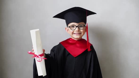 Smiling Little Boy Showing His First Diploma in Graduation Gown