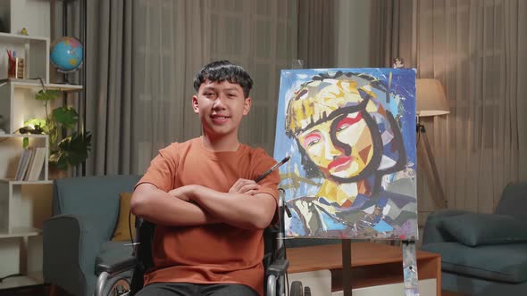 Asian Artist Boy In Wheelchair Cross His Arms And Smile While Painting A Girl On The Canvas